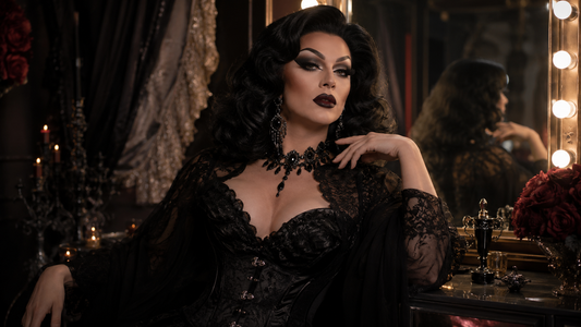 Drag queen con look dark glam, trucco drammatico, parrucca voluminosa, outfit nero scintillante e accessori importanti in un camerino teatrale.