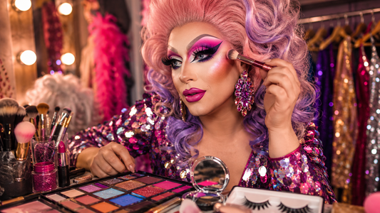 Trucco drag queen per principianti con pennelli, palette colorate, ciglia finte, rossetti e accessori glamour su un tavolo da preparazione.